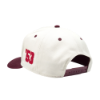 Left side view of "The Heritage Snapback", showing cream paneling with a burgundy "53" detail and snapback closure.